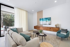 A modern living room with a sofa, armchairs, a coffee table, and a TV mounted on a wooden cabinet. - Villa Tropical Dawn (Bosques de Pinilla 10, Hacienda Pinilla)