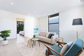 A modern living room with a sofa, armchair, and coffee table, a large window, and a view of a balcony.