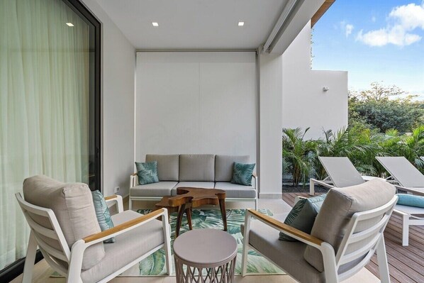 A modern outdoor seating area with a sofa and lounge chairs, a small round table, and a glass partition.