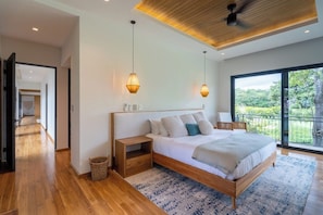 Ein modernes Schlafzimmer mit einem großen Bett, einem Holzkopfstück und Blick ins Freie durch eine Schiebeglastür.