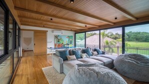 A spacious living area with a large sofa set, a bean bag, and a view of a lush landscape through large windows. - Seasons at Ceiba (Hacienda Pinilla)