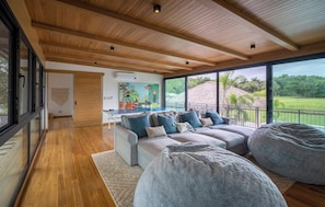 A spacious living area with a large sofa set, a bean bag, and a view of a lush landscape through large windows. - Seasons at Ceiba (Hacienda Pinilla)