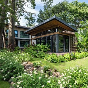 Ein modernes Haus mit einer überdachten Terrasse, umgeben von üppiger Vegetation und blühenden Pflanzen.