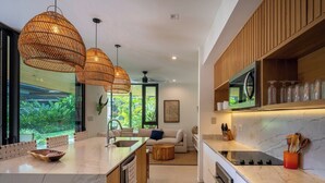 A modern kitchen with a marble countertop, wooden cabinets, and pendant lighting. - Seasons at Ceiba (Hacienda Pinilla)