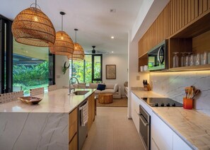 A modern kitchen with a marble countertop, wooden cabinets, and pendant lighting. - Seasons at Ceiba (Hacienda Pinilla)