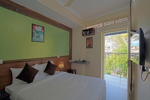 Habitación de hotel con cama, mesita de noche, televisor montado en la pared, ventana con vistas a la vegetación y puerta que da a un balcón.