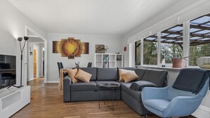Un salon moderne avec un canapé d’angle, un fauteuil à bascule et un coin repas.