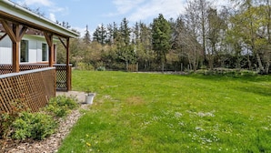 Un espace extérieur abrité, doté d’une terrasse en bois, d’une pelouse verdoyante et bordé d’arbres.
