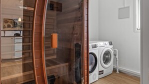 Une buanderie moderne équipée d’un lave-linge, d’un sèche-linge et d’un espace douche fermé par des parois en verre.
