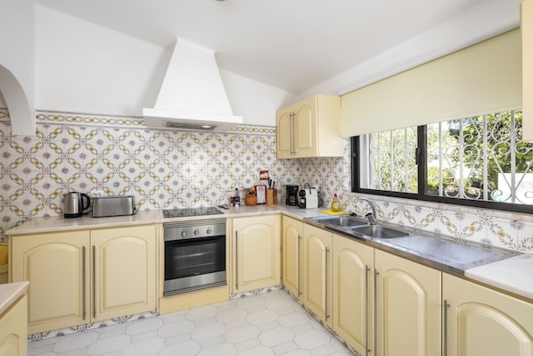 A kitchen with yellow cabinets, a stainless steel sink, and a window with a view of greenery. - Casa San Michel - holiday villa with private pool, air-conditioning and sea view (Lagoa)