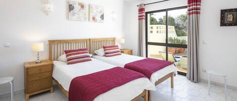 A bedroom with two beds, a wooden headboard, and a view of the outdoors through a large window.