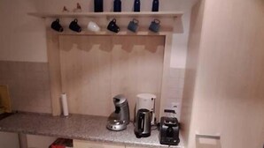 A compact kitchen with a countertop, a coffee maker, a kettle, and a refrigerator.
