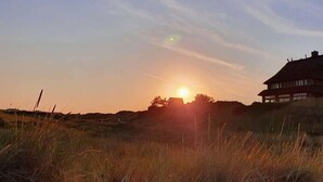 A sunset over a grassy field with a house in the background.
