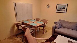 A small, cozy room with a wooden table and chairs, a gray sofa, and a framed picture on the wall.