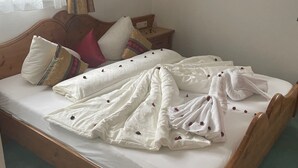 Un letto rifatto con lenzuola bianche e una coperta a motivi floreali, una testiera in legno e un comodino con una lampada.