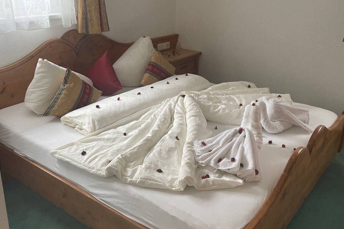 A neatly made bed with white linens and a floral-patterned blanket, a wooden headboard, and a nightstand with a lamp.
