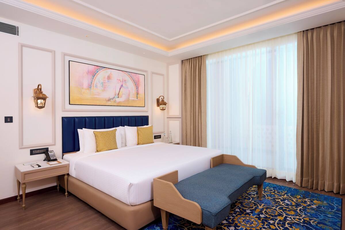 A hotel room with a large bed, a bedside table with a phone, and a wall-mounted lamp.