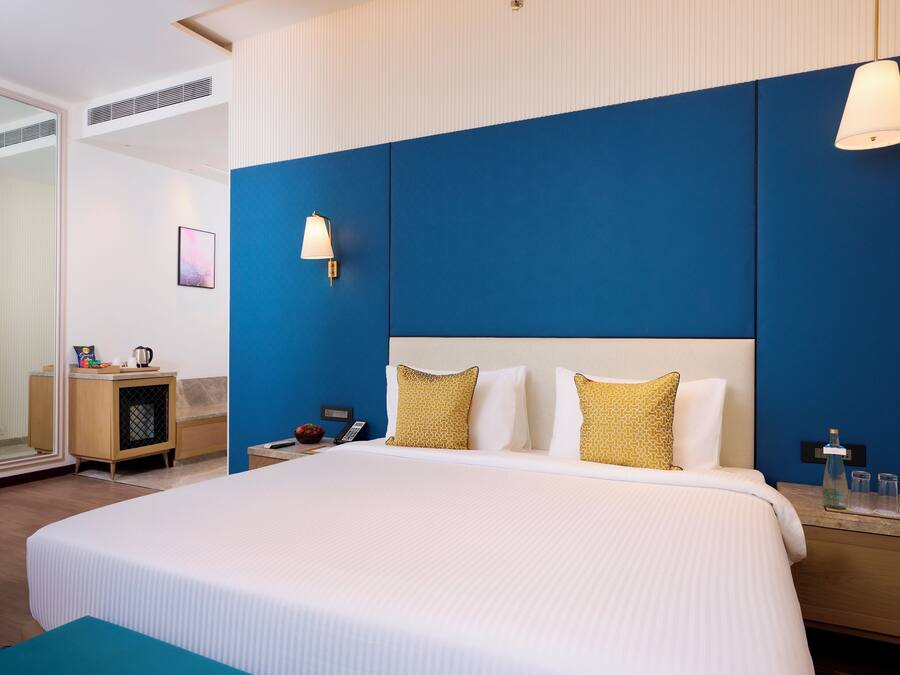Une chambre d’hôtel avec un grand lit, une table de chevet avec une lampe, une petite armoire en bois et un miroir.