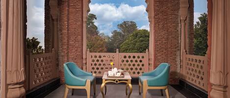 A balcony with two turquoise chairs, a table with a tea set, and a view of trees through a star-patterned fence.