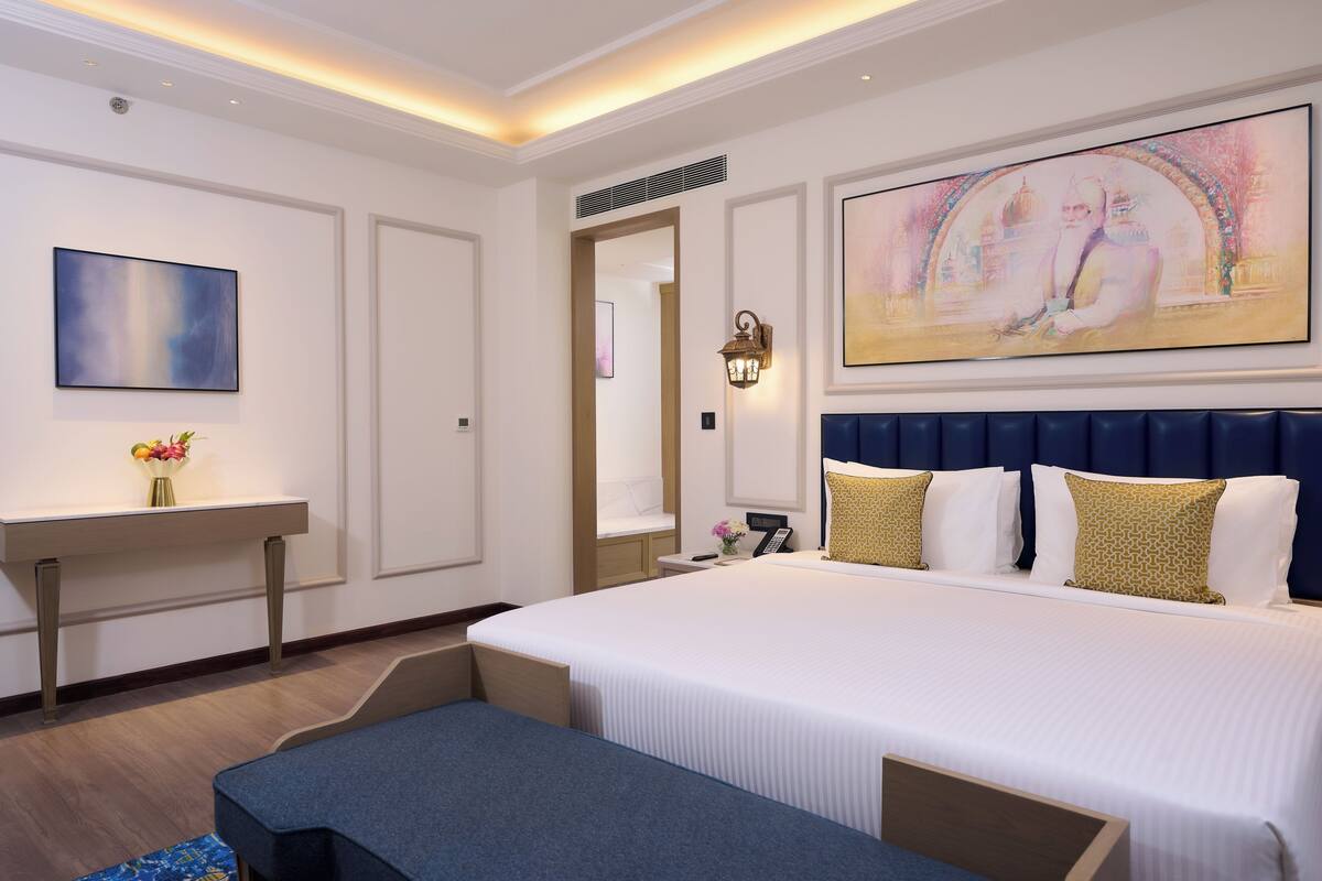 A hotel room with a large bed, a desk, a chair, and a painting on the wall.