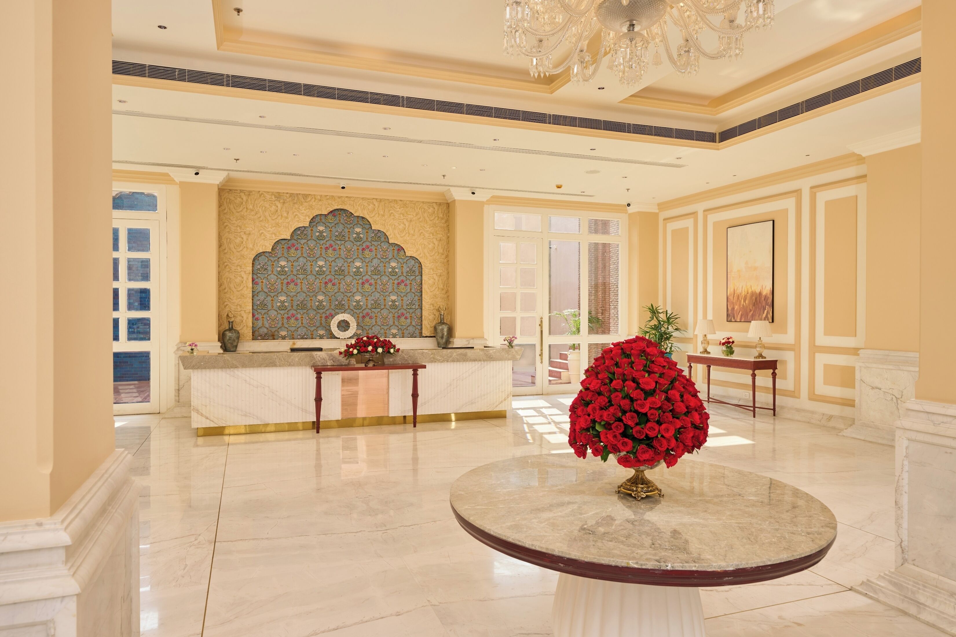 A spacious lobby with a marble reception desk, a decorative wall, and a large floral centerpiece.