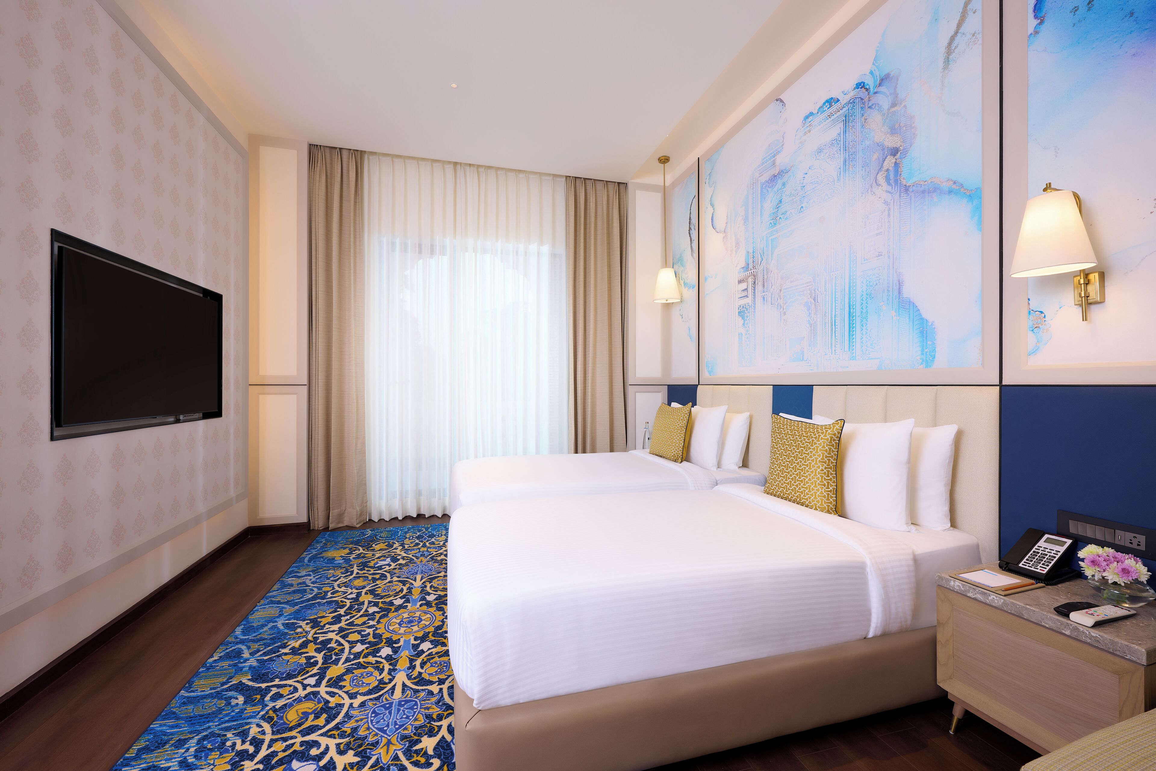 A hotel room with two beds, a flat-screen TV, a nightstand with a phone, and a large abstract painting on the wall.