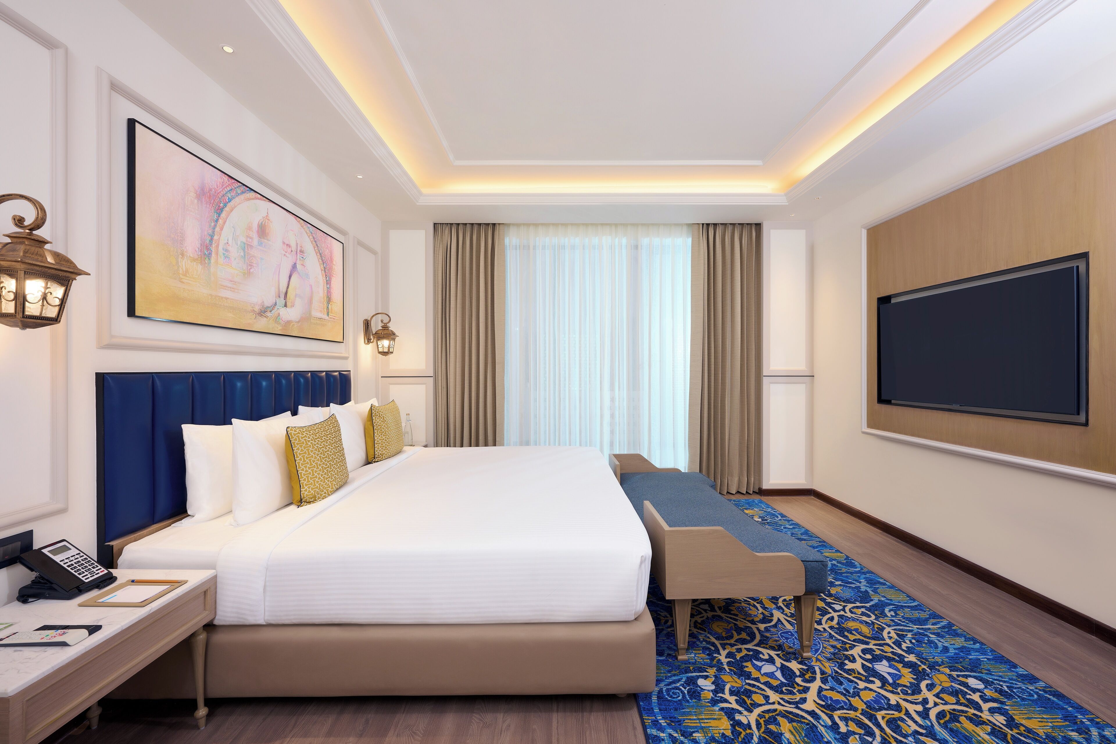 A hotel room with a large bed, a desk with a telephone, a flat-screen TV, and a large window with curtains.