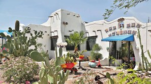 A building with a white exterior and a blue awning, surrounded by cacti and desert plants. - Modern Desert Escape | Pool, Gym, W/D, Parking (Phoenix)