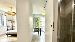 A modern bathroom with a glass shower enclosure, a wooden floor, and a view of a balcony with greenery.