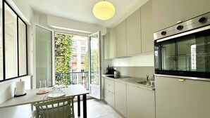 A modern kitchen with a built-in oven, a dining table with chairs, and a view of a balcony with greenery.