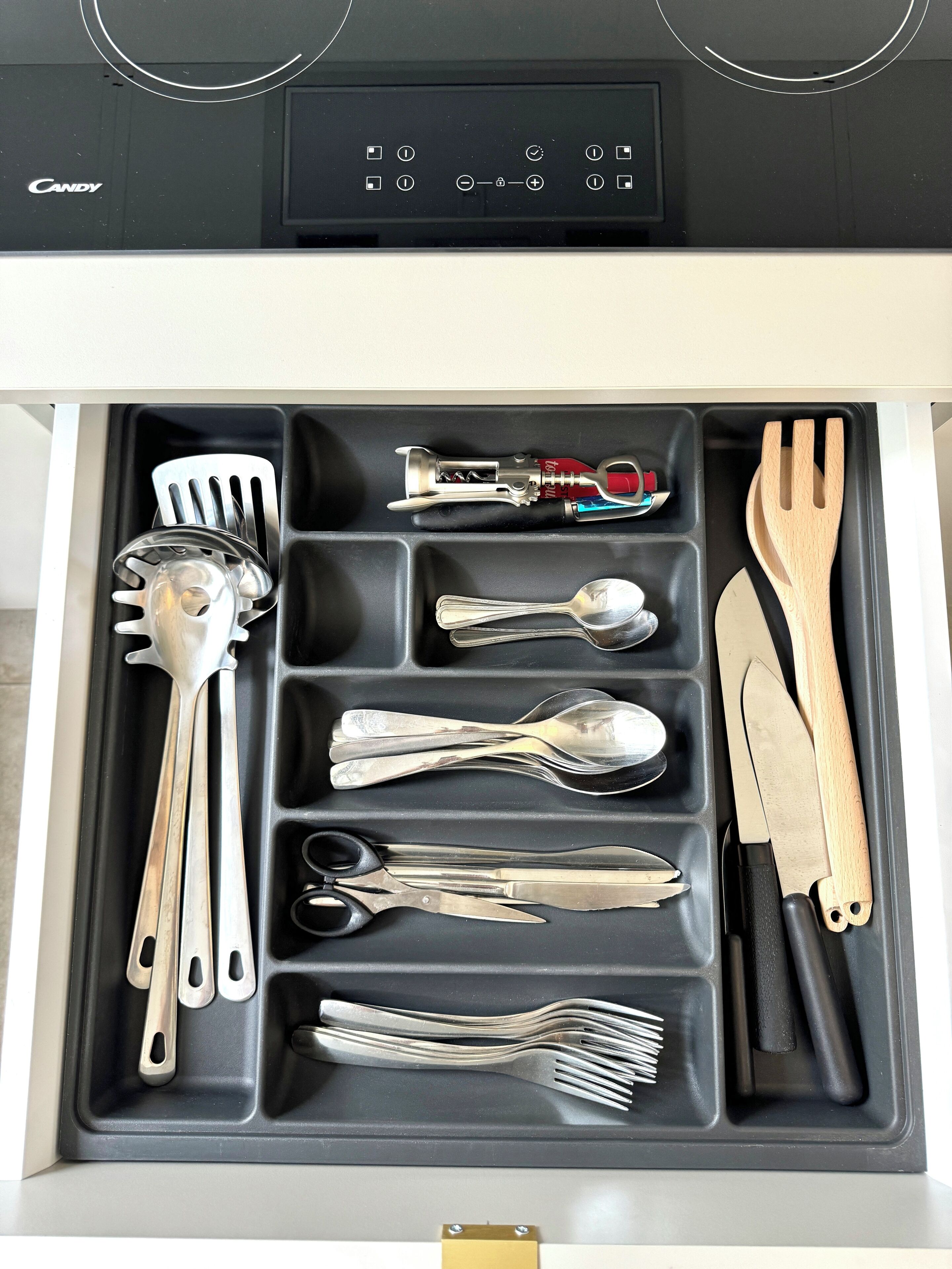 Un tiroir contenant divers ustensiles de cuisine, notamment des cuillères, des fourchettes, une spatule et un couteau.