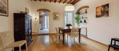 Uma sala de jantar com mesa de madeira, cadeiras e um candelabro. Há um armário de madeira e um banco no canto.