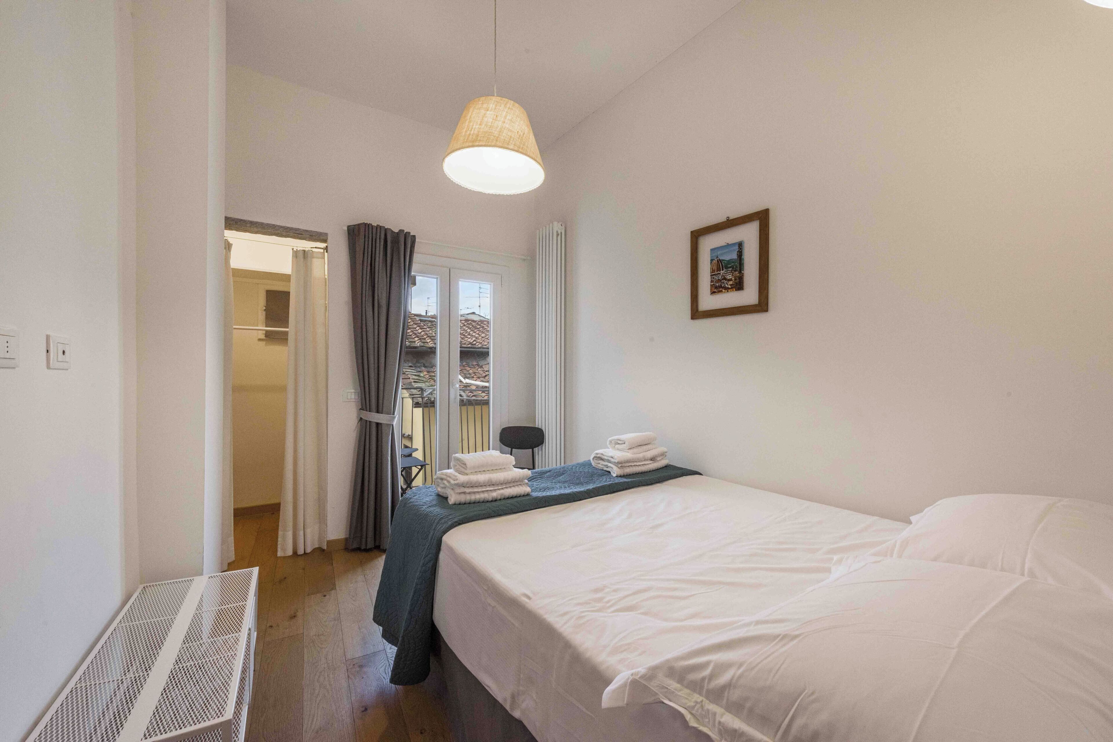 A bedroom with a bed, a radiator, a picture on the wall, and a window with curtains.