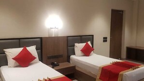 Una camera d'albergo con due letti, ognuno con un cuscino rosso, un comodino e una lampada.