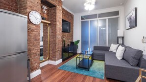 Un salon moderne avec un mur en briques, un canapé gris, une table basse et une grande fenêtre.
