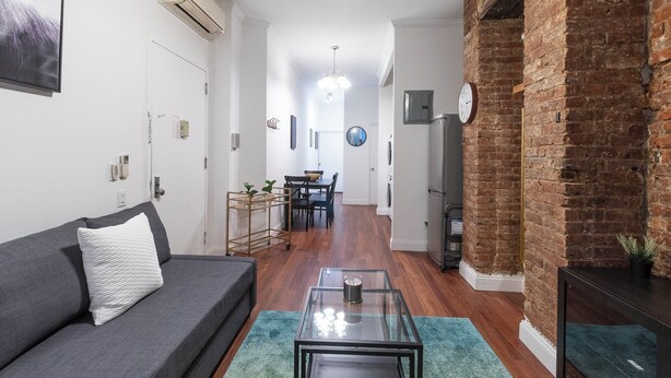 Un salon moderne avec un canapé gris, une table basse en verre et un mur en briques.