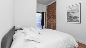 Une chambre à coucher avec un lit, du linge de lit blanc, un mur en briques et un tableau encadré accroché au mur.
