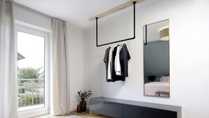 A modern bedroom with a large window, a bedside table, a mirror, and a hanging clothes rack.