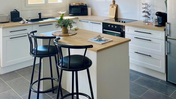 Une cuisine moderne avec un îlot central, des tabourets de bar noirs, un luminaire suspendu noir et des meubles de rangement blancs.