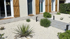 Une maison avec un toit en tuiles, des portes en bois et un jardin recouvert de gravier, agrémenté de plantes.