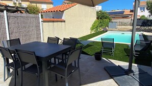 Une terrasse avec une piscine, du mobilier d’extérieur et un espace abrité.