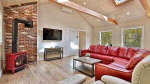 A spacious living room with a red leather sofa, a wooden coffee table, and a red wood-burning stove. - Experience the charm of Peak Hill Home,  Entire home in Killington/Pittsfield, Vermont (Pittsfield)