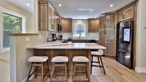 A modern kitchen with wooden cabinets, a large island with stools, and stainless steel appliances. - Experience the charm of Peak Hill Home,  Entire home in Killington/Pittsfield, Vermont (Pittsfield)
