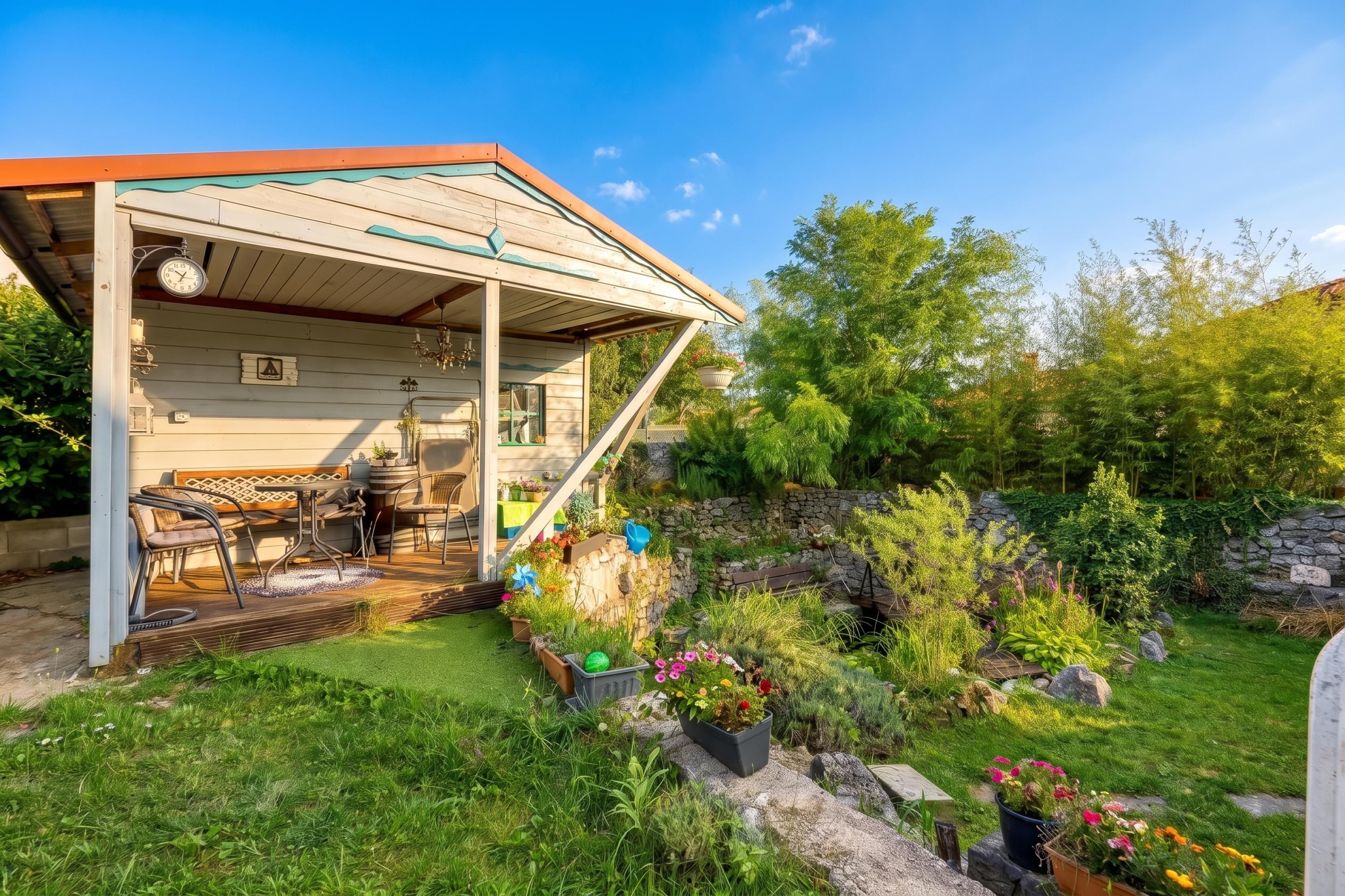 A wooden house with a covered porch, outdoor seating, and a garden with various plants and a stone wall.
