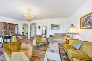 A spacious living room with a chandelier, sofas, a coffee table, and a dining area with a cabinet. - Villa Salamander Suite - Garden & EV Charger (Komen)