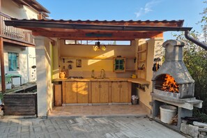 An outdoor kitchen with a stone oven, wooden cabinets, and a pergola. - Villa Salamander Suite (Komen)