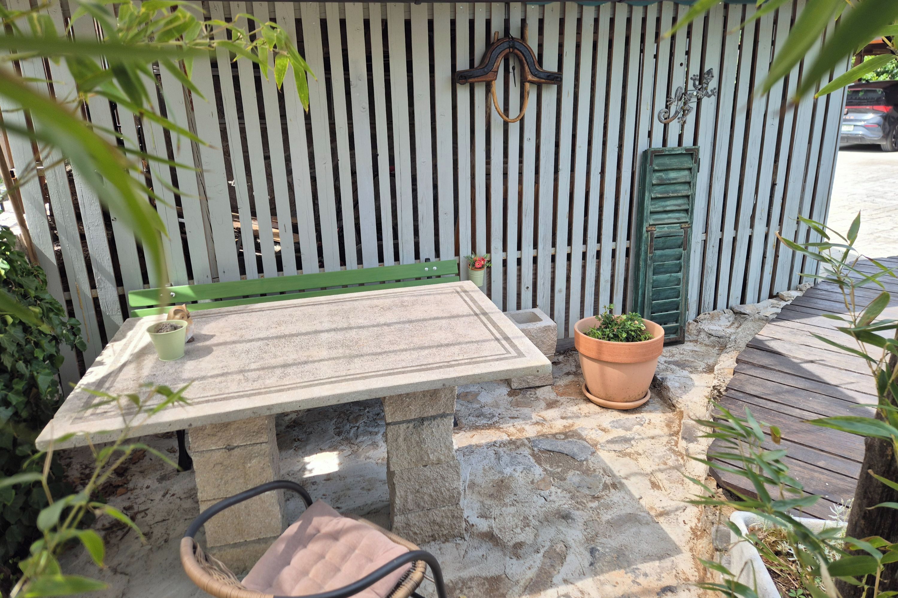 Un tavolo in pietra con una panchina verde, piante in vaso e un pontile in legno.