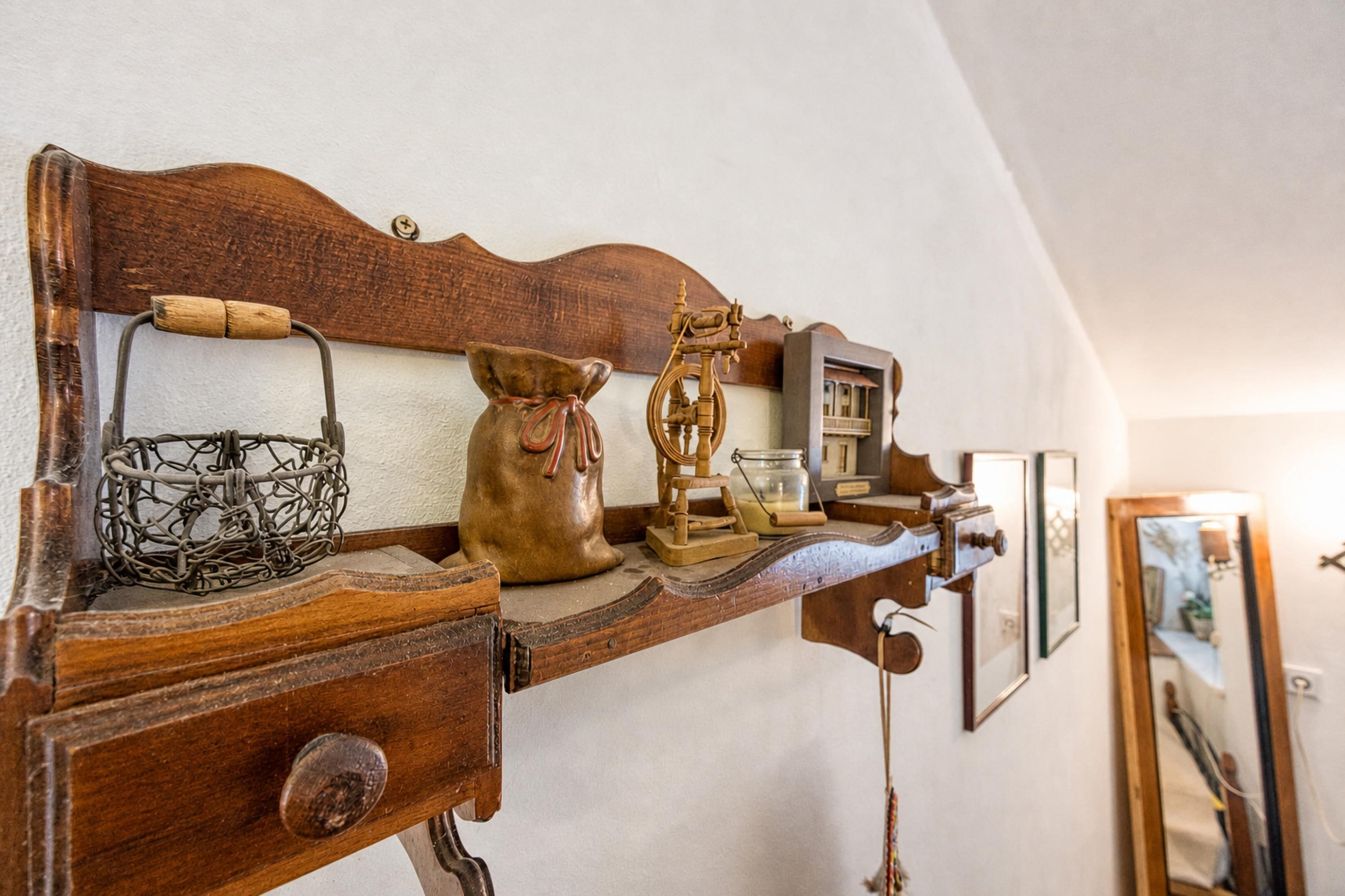 A wooden shelf with various antique items including a metal basket, a ceramic jug, and a wooden clock.