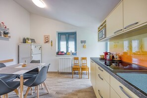 A compact kitchen with a dining area, a refrigerator, a microwave, and a window with blinds.