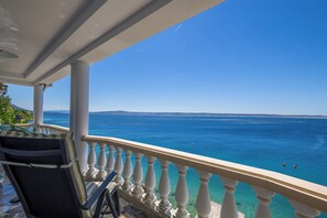 A balcony with a clear view of the sea, white balustrades, and a chair.